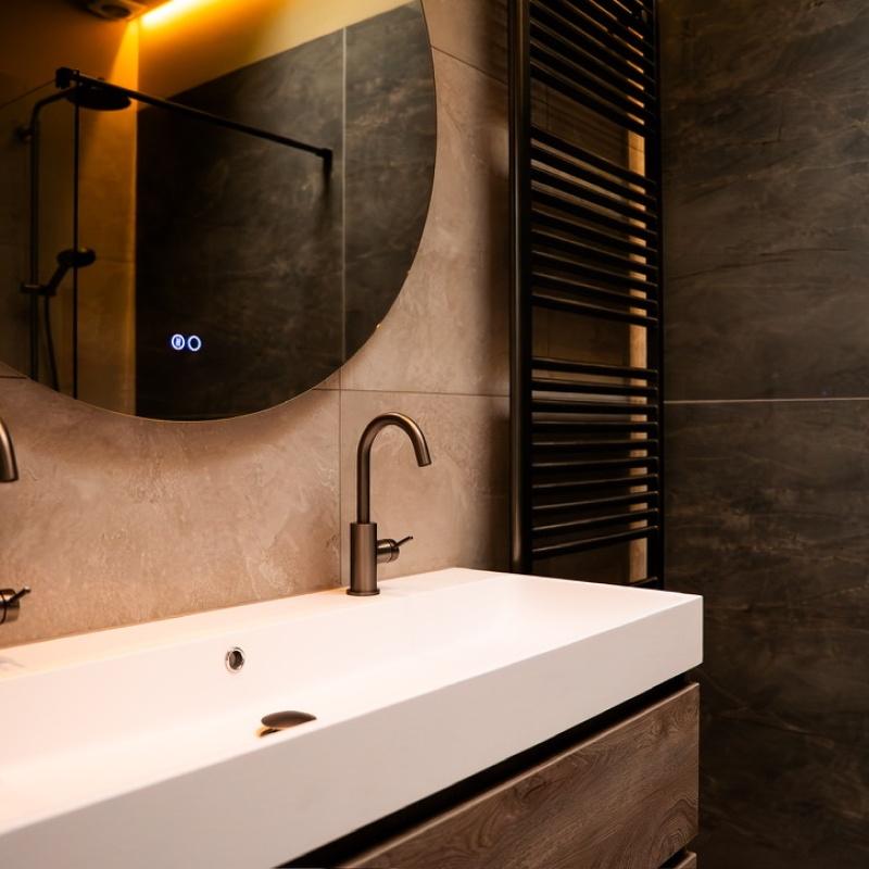 Bathroom with double sink, round backlit mirror and black towel radiator, finished with dark marble-effect tiles as part of the A+++ renovation in The Hague