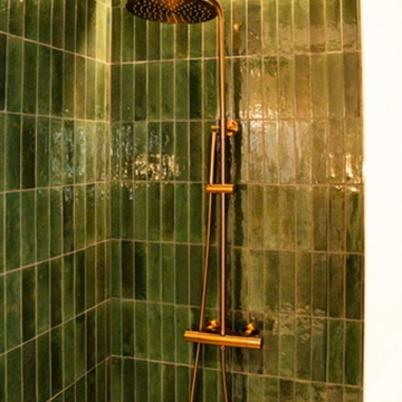 Walk-in shower with green tiles and a bronze-coloured rain shower in the teenagers' bathroom
