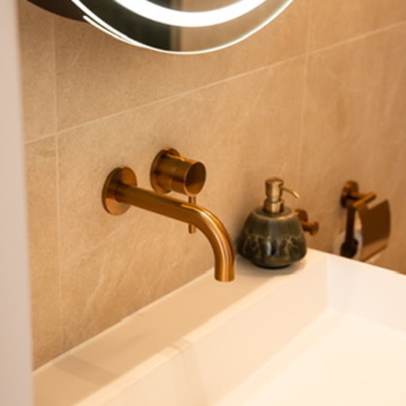 Small basin with a gold tap and beige vertical tiles in the toilet