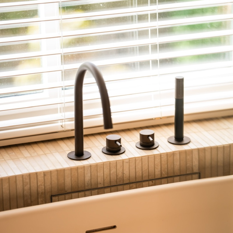 Freestanding bath with a black deck-mounted tap by the window