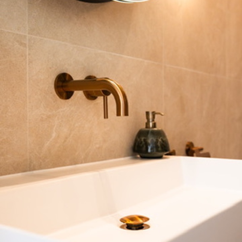 Washbasin with a gold tap beneath a round illuminated mirror