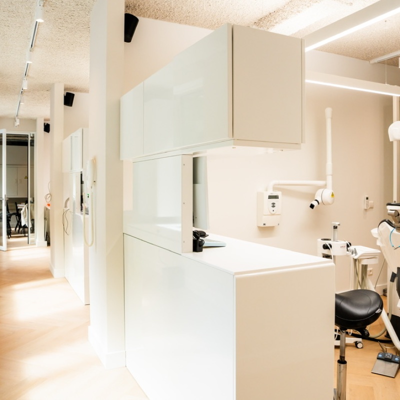 Behandelkamer met witte kastenwand, tandartsstoel en röntgenapparaat
