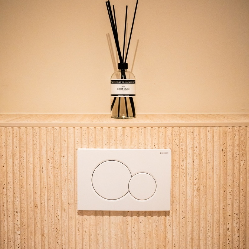 Detail van de toiletruimte met geurstokjes en spoelpaneel op een travertin wand