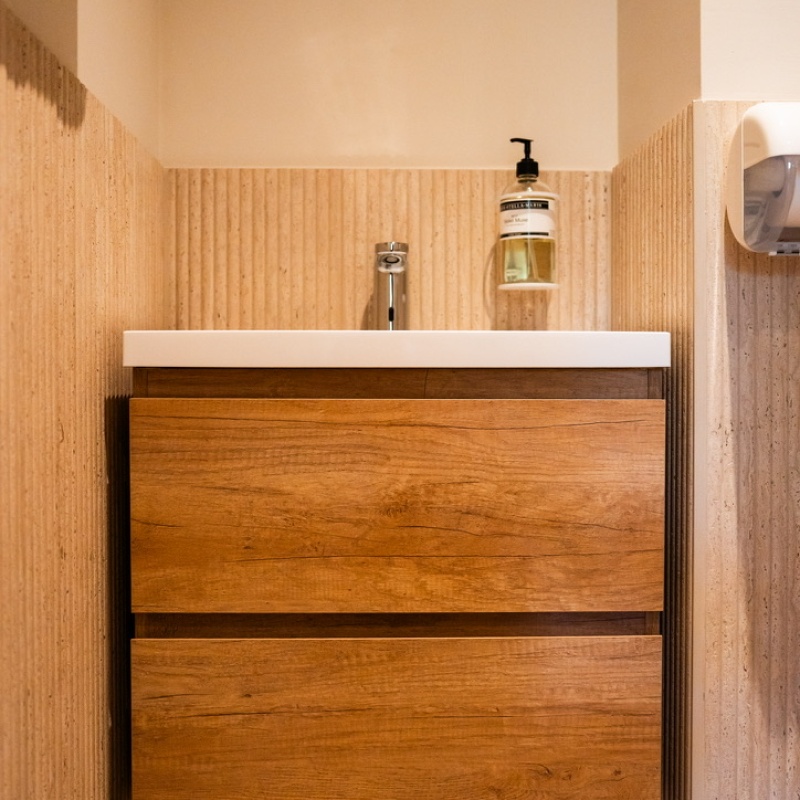 Toiletruimte met houten wastafelmeubel en travertin wandbekleding